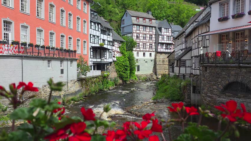 Half timbered house of Monschau in the Eifel region of western Germany. Red flowers in a gentle breeze and flowing river.