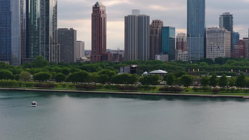 Urban expanse of downtown Chicago with modern high rise towers and verdant parkland lining Lake Michigan waterfront under overcast sky in Illinois