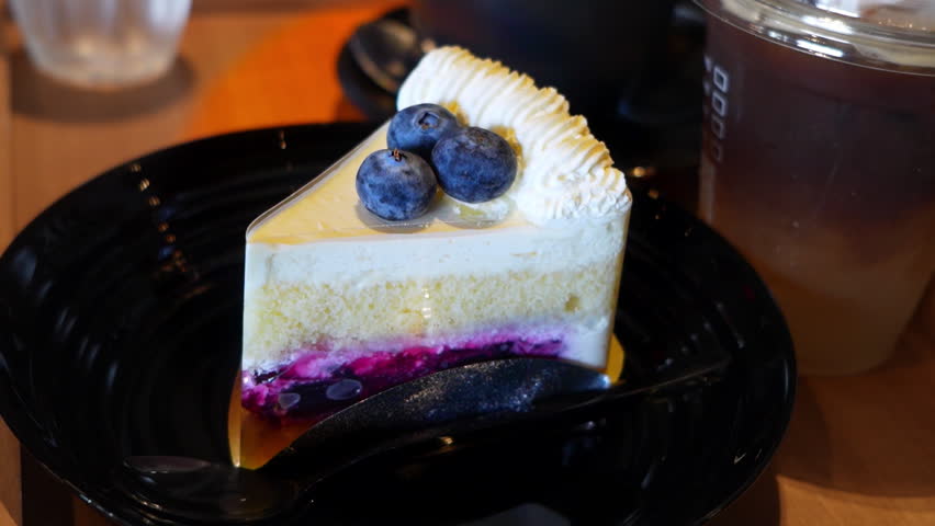 Slice of homemade fresh blueberry cheesecake with rich topping on table in modern cafe