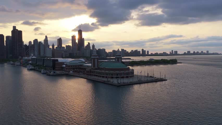 Chicago Navy Pier with panoramic cityscape featuring John Hancock Center and downtown skyline during warm sunset above Lake Michigan with sun reflecting in water