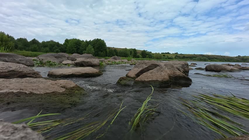 Scenic river rapids with stones under a cloudy sky, surrounded by green trees