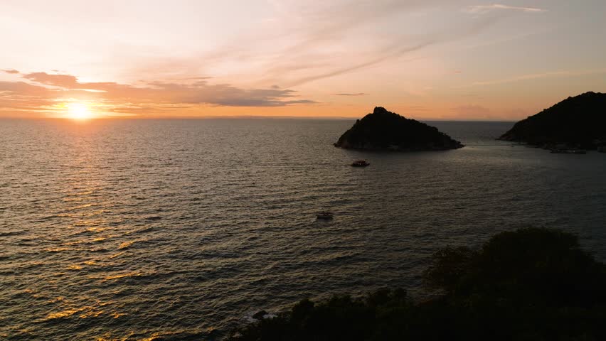 Golden sunset over calm sea with small island silhouettes and boats in view. Koh Tao, Thailand.