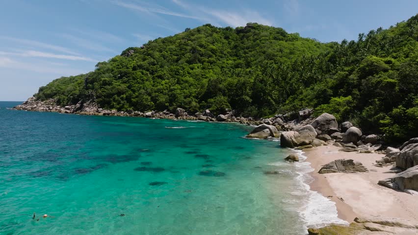 Turquoise bay surrounded by green hills and rocky shore under clear sky. Koh Tao, Thailand.