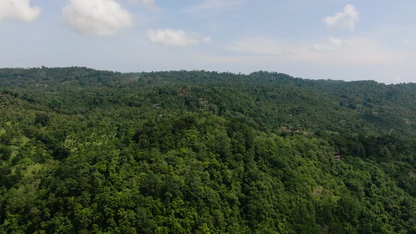Expansive view of lush green forested hills under a blue sky with scattered clouds. Ko Samui, Thailand.