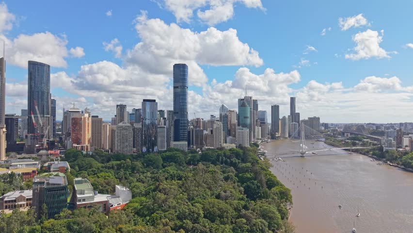 Brisbane city skyline overlooking the Brisbane River and Kurilpa Bridge beneath dramatic clouds on a bright afternoon in Queensland.