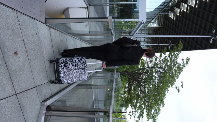 Walking on a pathway with a bag near a modern building and trees on a cloudy day