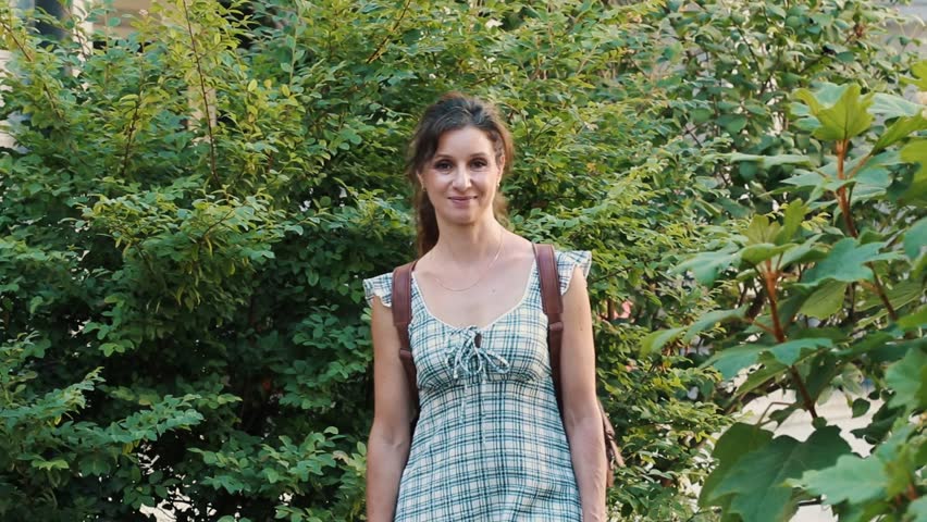 Charming adult woman with a backpack strolling through a lush green park. The beautiful lady enjoys a sunny day walking outdoors