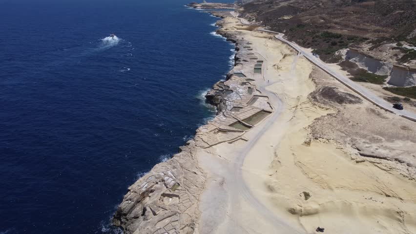 Xwejni s centuries-old salt pans unfold along the rugged coast of Zebbug, Gozo, geometric pools and vivid Mediterranean blues in a sweeping summer Aerial view. High quality 4k footage