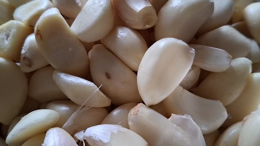 A detailed close up view showing a large group of fresh, raw, peeled garlic cloves resting together in a pile, ready for culinary use.