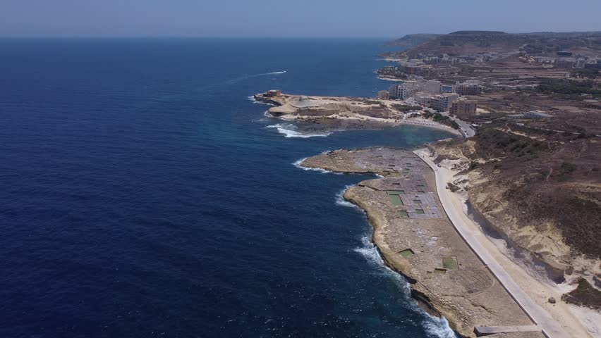 Xwejni s centuries-old salt pans unfold along the rugged coast of Zebbug, Gozo, geometric pools and vivid Mediterranean blues in a sweeping summer Aerial view. High quality 4k footage