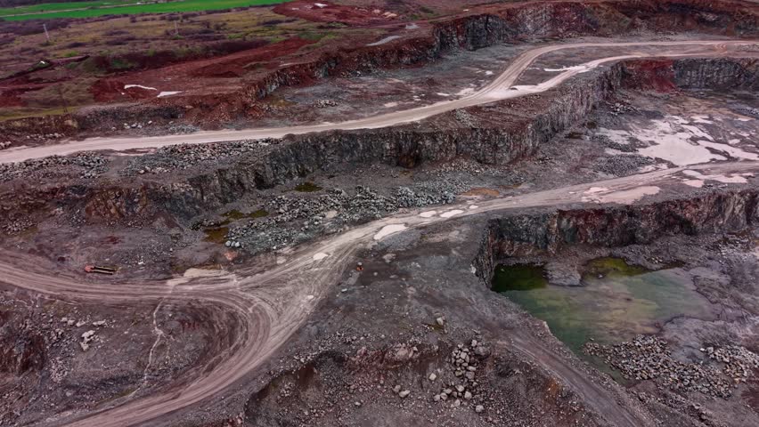 The scene shows an industrial granite quarry with large stone walls and dirt paths. Water pools gather in some areas. Machines and workers may be present. The landscape is rugged.