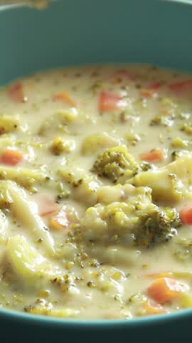 Close-up of creamy broccoli cheddar soup served in a rustic ceramic bowl, topped with black pepper and fresh broccoli florets