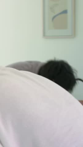 Vertical video: Turning faucet, man in gray robe cupping water, rinsing face at bathroom sink. Basin, tap, mirror, sunlit, modern, couple, vertical video