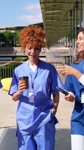 Multiracial group of medical students and health professionals enjoying a coffee break, walking and talking together outside a modern hospital building on a sunny day in the city
