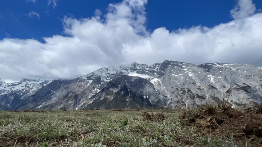 A Timelapse of the Jade Dragon Snow Mountain under cloudy sky, with grassy field in the foreground near Lijiang, Yunnan China