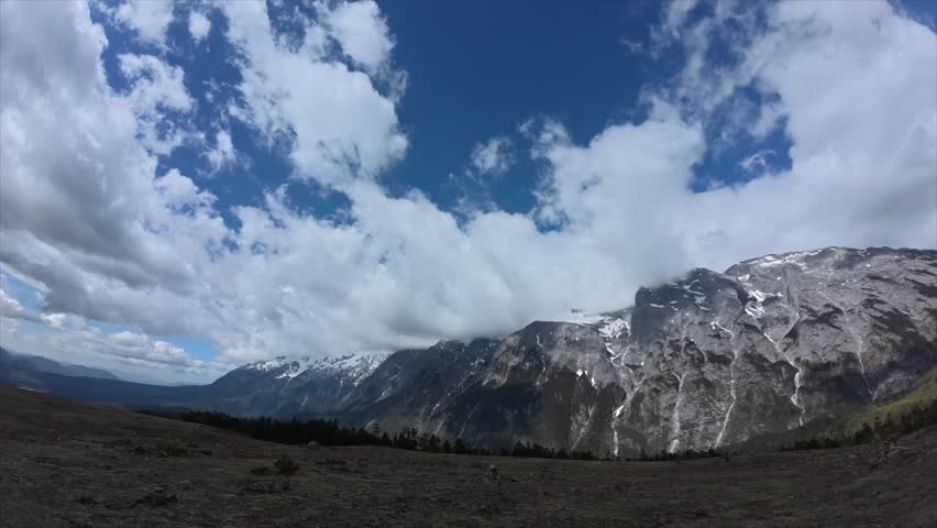 A timelapse of the Jade Dragon Snow Mountain under cloudy sky, with grassy field in the foreground near Lijiang, Yunnan, China