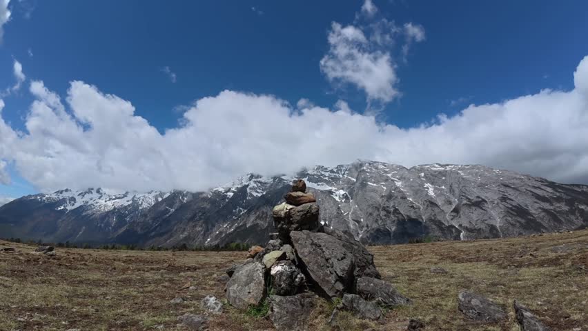 A timelapse of the Jade Dragon Snow Mountain under cloudy sky, with stone balance formation in the foreground near Lijiang, Yunnan, China