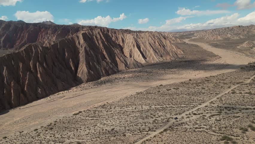 Aerial view of the rugged Valles Calchaquies desert landscape with dramatic mountain ridges, arid plains, and a winding dirt road in San Carlos, Salta, Argentina.