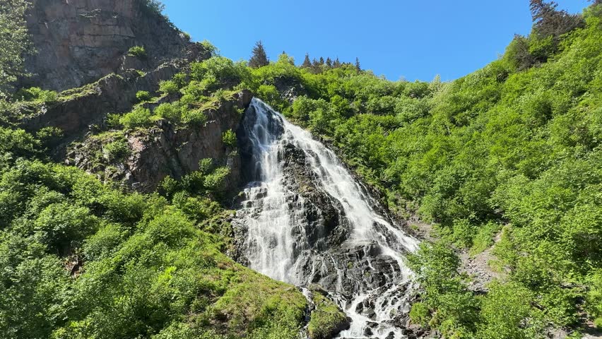 Waterfall.Mountain river flows through trees in landscape with snow-capped peaks nearby at daytime in Canada