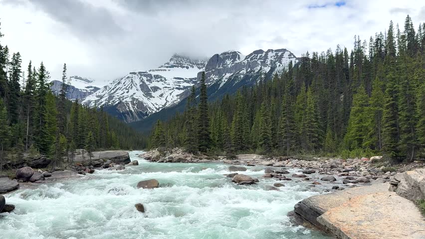 Waterfall.Mountain river flows through trees in landscape with snow-capped peaks nearby at daytime in Canada