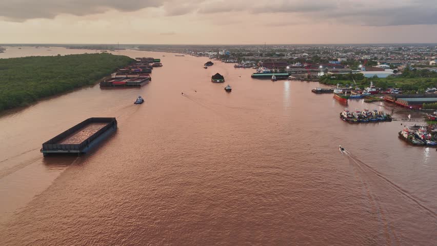 Aerial view of Barito River with coal barges and boats navigating the waterway at sunset in Banjarmasin, Kalimantan Selatan, Indonesia.