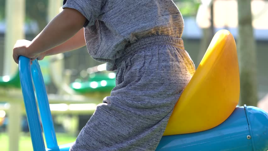 A close up view of a person sitting on a bright blue and yellow seesaw at a local outdoor playground.