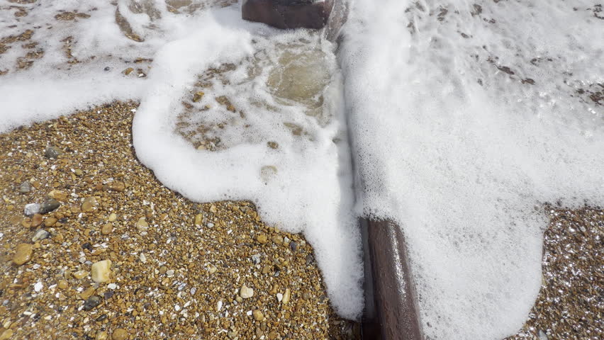 Person touching ocean foam by pipe panning