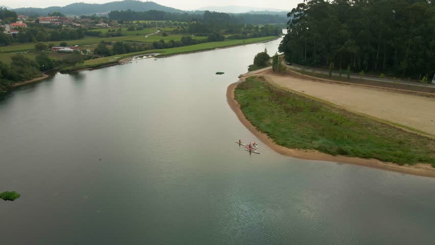 Aerial view of people canoeing on the calm waters of the Cavado River near a sandy bank with lush green trees in the background in Esposende, Braga, Portugal.