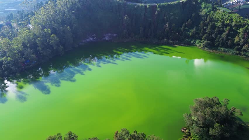 Aerial drone footage of Telaga Warna (Color Lake) on the Dieng Plateau, Central Java, Indonesia, captured during the late afternoon golden hour. Famous for its naturally changing water colors caused by sulfur minerals and sunlight reflection