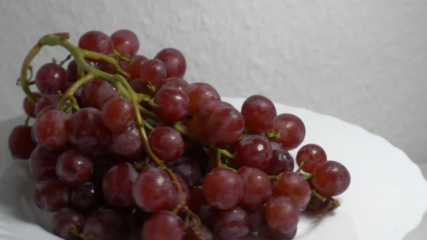 Close-up of a fresh bunch of red grapes rotating on a white turntable, showcasing their ripe berries and glossy texture under studio lighting.