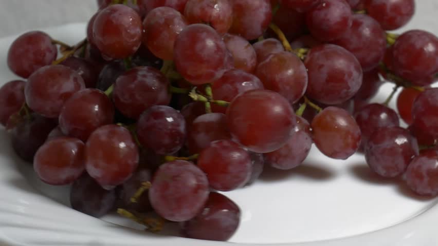 Close-up of a fresh bunch of red grapes rotating on a white turntable, showcasing their ripe berries and glossy texture under studio lighting.