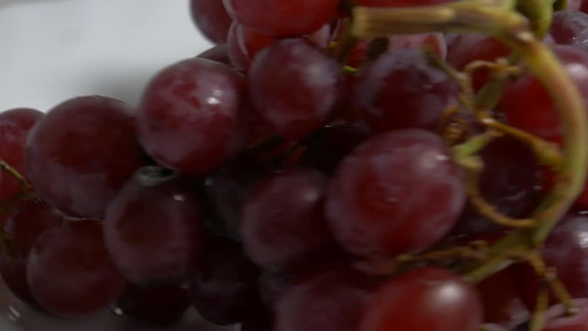 Close-up of a fresh bunch of red grapes rotating on a white turntable, showcasing their ripe berries and glossy texture under studio lighting.