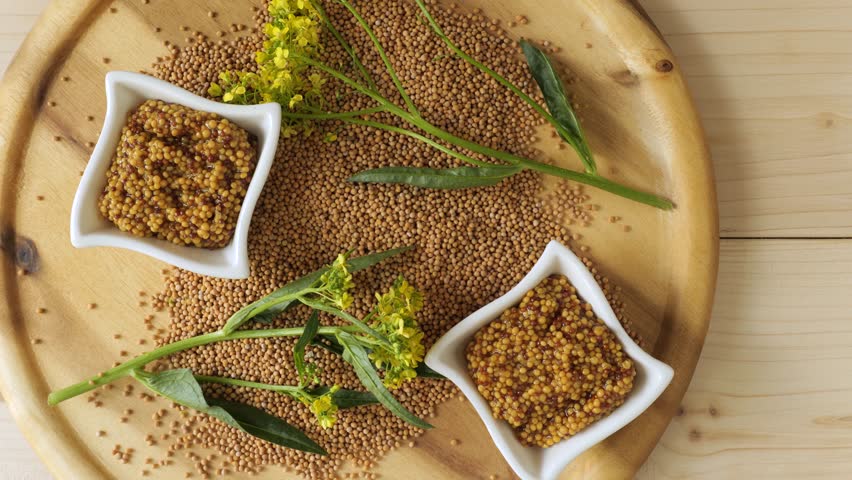 Wholegrain mustard in bowls with fresh mustard flowers and seeds on a round wooden plate