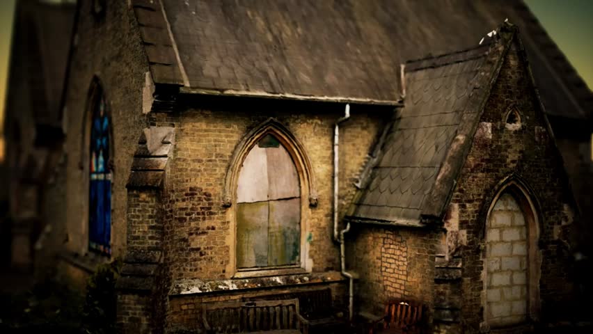 An old abandoned brick church with boarded up windows and colorful stained glass stands under a gloomy dramatic sky.