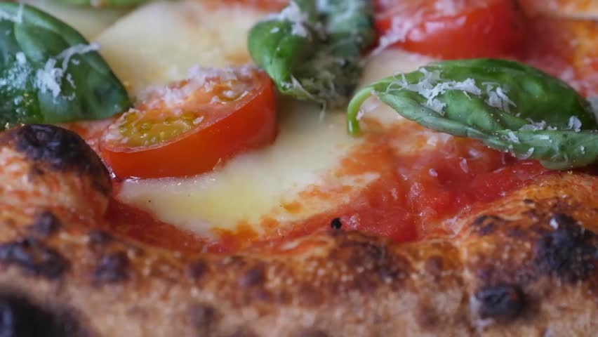 A macro view of a freshly baked Italian Pizza Margherita, featuring a thick, wood-fired crust with leopard spotting, molten mozzarella cheese, sliced cherry tomatoes, and aromatic fresh basil leaves.