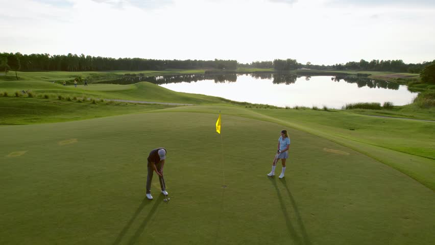 Drone view of young golfers swing clubs together on a scenic golf course. Attractive man and woman enjoy outdoor recreation with light exercise and sport lifestyle while playing golf at course ground.