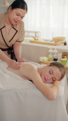 Beautiful woman getting back massage treatment with oil at beauty spa. Attractive girl lying down on massage bed receiving relaxing physiotherapy service from masseuse for body wellness in spa clinic.