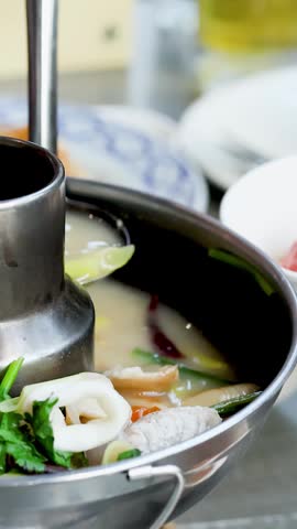 Close-up of a ladle pouring hot seafood soup into a bowl at a restaurant.