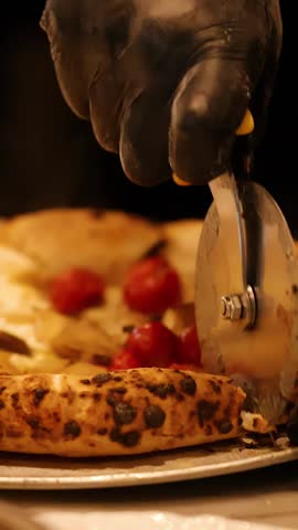 Close-up of gloved hands cutting sourdough pizza with cherry tomatoes in a restaurant kitchen.