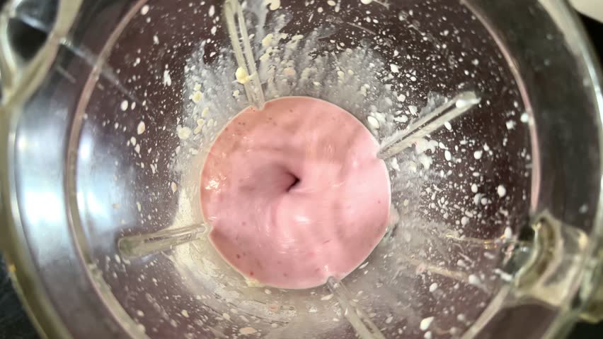 Overhead view of a pink glazed donut being dusted with powdered sugar captured from above showing the sweet dessert preparation process in a bakery style setting.