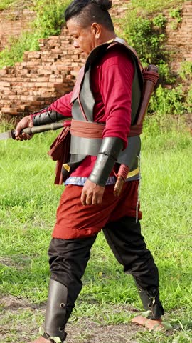Two soldiers in traditional armor practice martial arts with swords near ancient brick ruins.