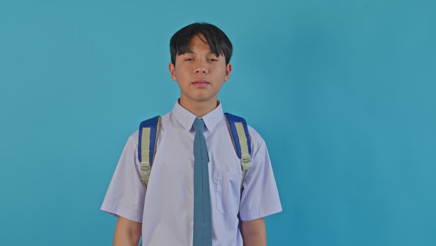 Indonesian high school student looking through magnifying glass with funny expression on blue background
