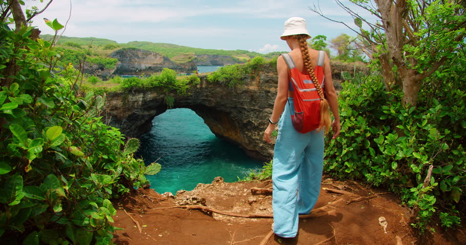 Tourist with backpack walking at Broken Beach natural arch in Nusa Penida Bali