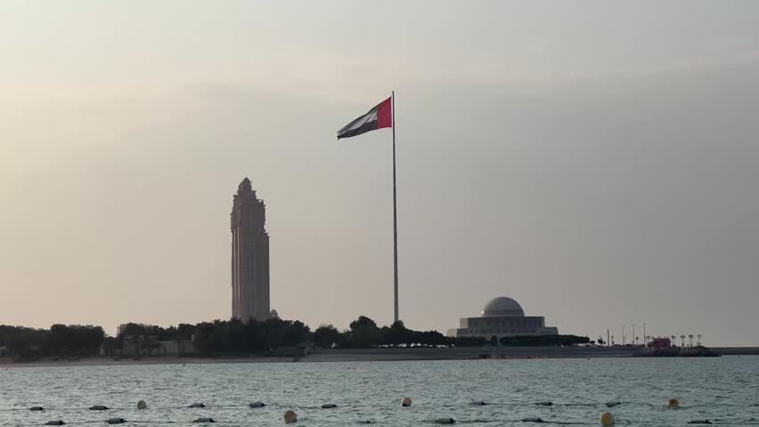 United Arab Emirates flag waving in the sky. Flag in the capital of UAE, Abu Dhabi. Flag of the UAE seen outdoors over the gulf in Dubai. 
