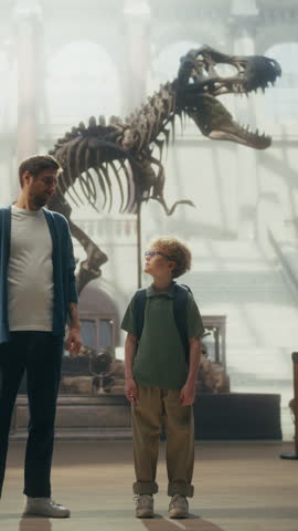 Vertical Screen: Natural History Museum With a Father and Young Son Holding Hands, Watching and Learning About a Giant T-rex Dinosaur Skeleton. Family Vacation Fun and Education