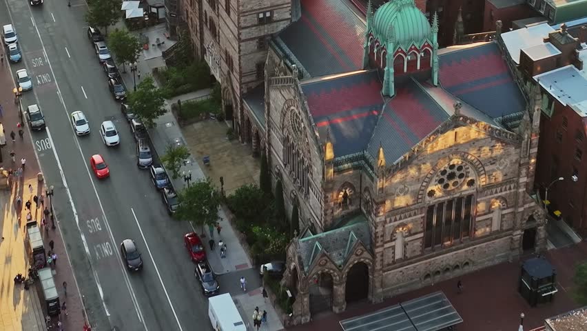 An aerial view of a historic building in a city in the USA. The shot captures the roof and surroundings, highlighting the busy street below in late afternoon light.