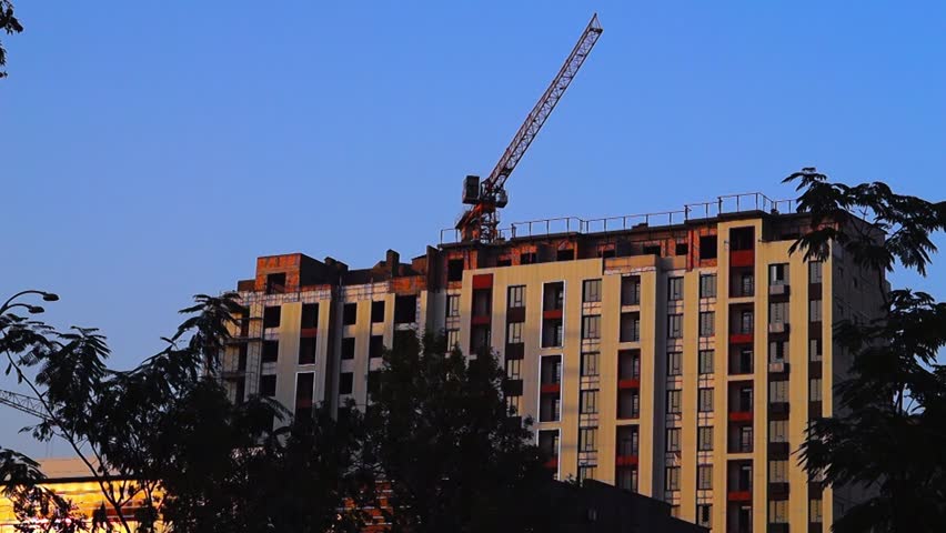 A tower crane rotates its boom. A construction site with a multi-story residential building under construction, finishing work on the facade