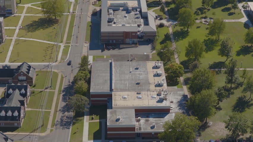 Aerial drone footage showing a college campus quad with green trees and academic buildings under clear midday light in Clarksville Arkansas.