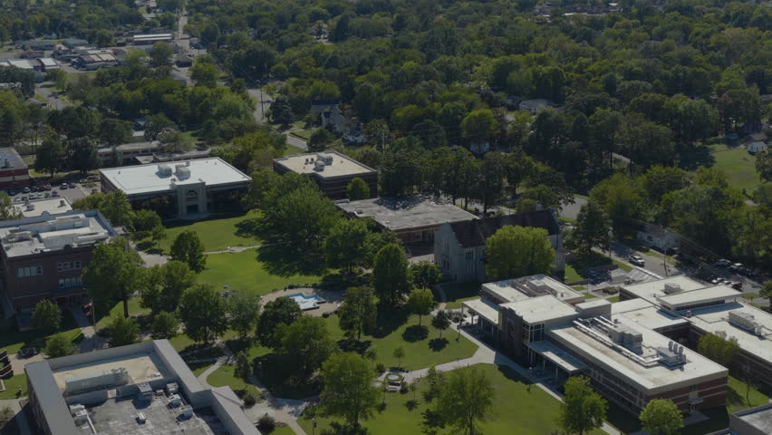 Aerial drone footage of a college campus in Clarksville, Arkansas, showing green trees, a central mall fountain, and academic buildings on College Hill during midday.