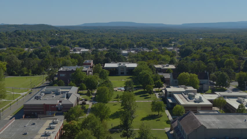 Aerial drone footage captures a midday view of a college campus quad surrounded by green trees and buildings in the Ozark foothills of Clarksville Arkansas.
